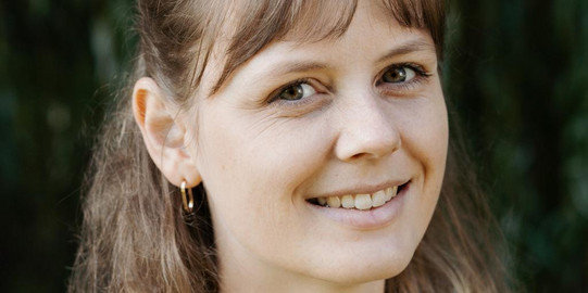 Frau mit hell braunen lockigen Jahren lächelt seitlich zur Kamara